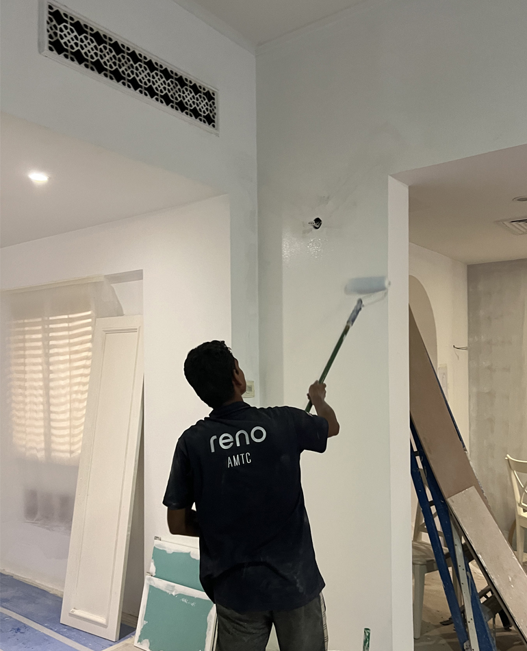 painter in AMTC reno t-shirt applying white paint to an interior wall with a roller